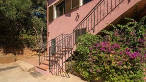 A pink building with a staircase, a window, and a bush with purple flowers. - Holiday Home 'Casa Teresa' with Mountain View, Balcony, and Air Conditioning (Iglesias)
