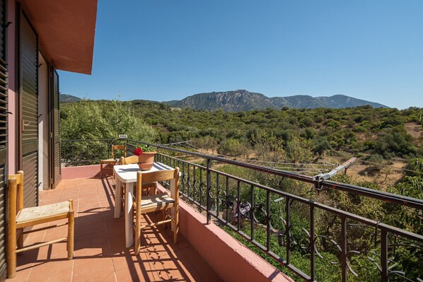 Un balcón con una mesa y sillas, una planta en maceta y vistas de un paisaje montañoso.