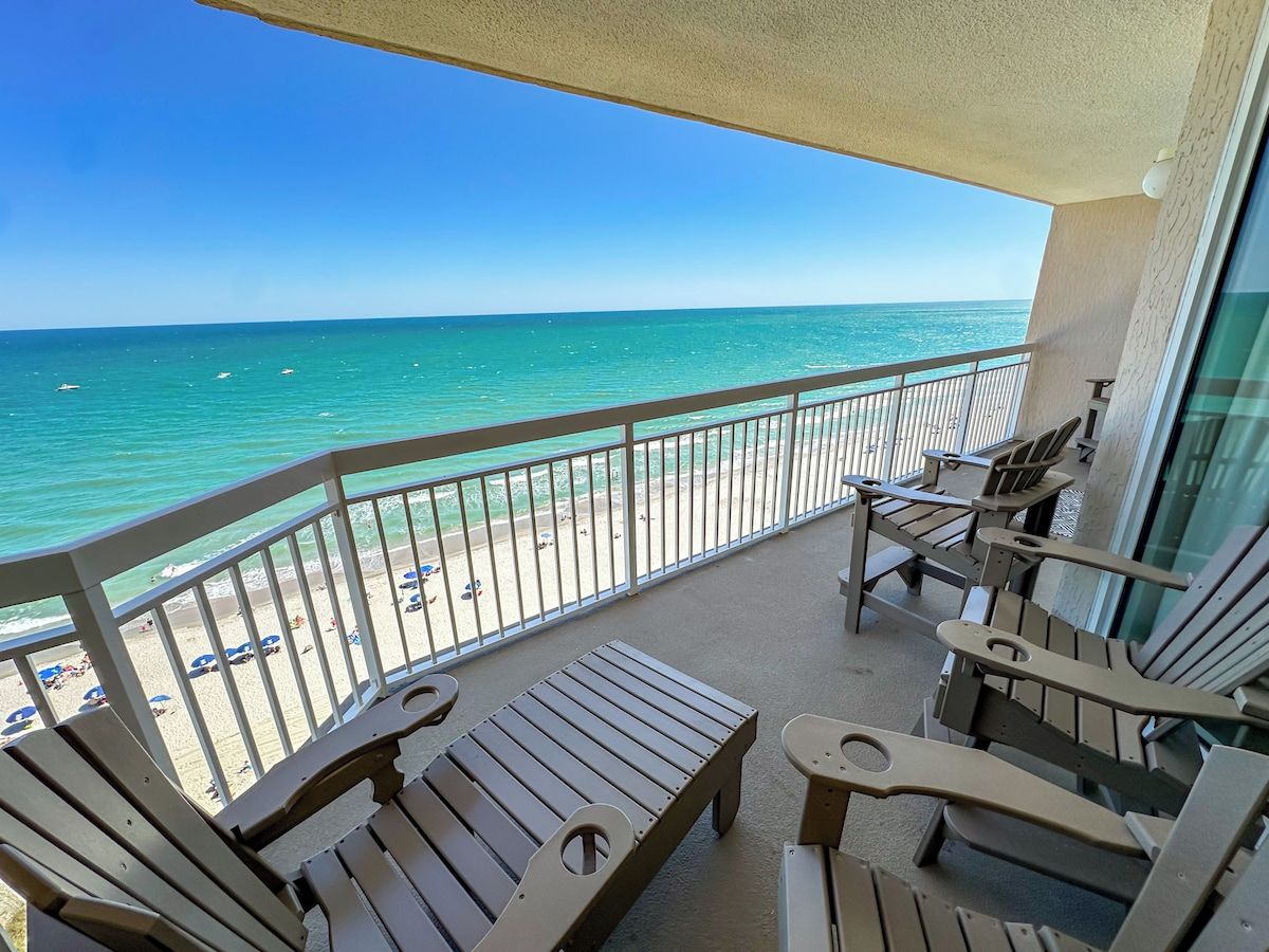 A balcony with wooden furniture overlooking a beach.