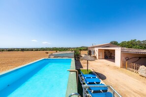 Ein Schwimmbecken mit Liegestühlen, einer überdachten Terrasse und Blick auf die Landschaft.
