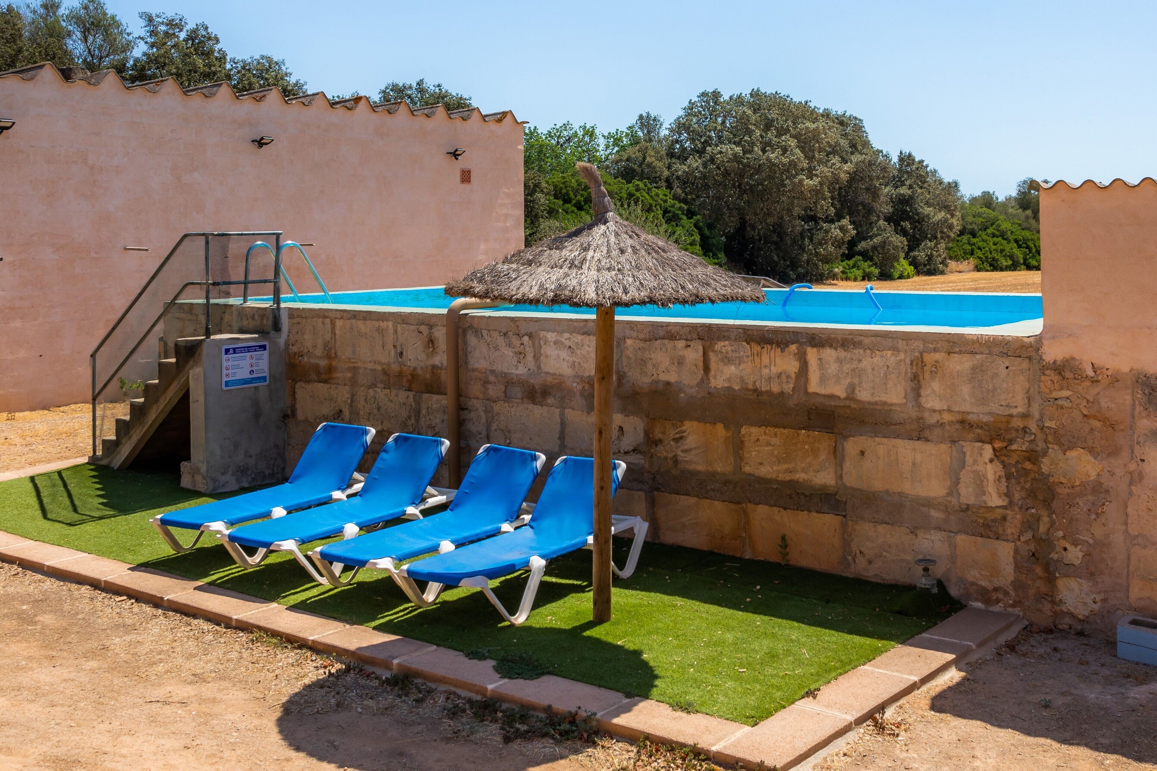 Une piscine à l’eau bleue, entourée de murs en pierre et surmontée d’un parasol en chaume.