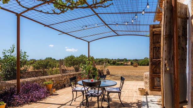 A covered patio with a table and chairs, surrounded by stone walls and potted plants.