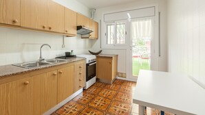 Una cocina con armarios de madera, encimera blanca, estufa y ventana con cortinas.