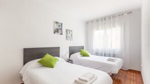 Una habitación de hotel con dos camas, una ventana con cortinas translúcidas y suelo de baldosas.