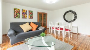 Una sala de estar con un sofá, una mesa de centro de vidrio, una mesa de comedor con sillas y un espejo en la pared.