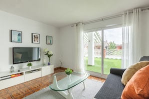 Un salon équipé d’un téléviseur, d’une table basse en verre, d’un canapé et d’une porte-fenêtre coulissante donnant sur un jardin.