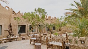 Un patio exterior con paredes de piedra rústica, bancos de madera y palmeras.