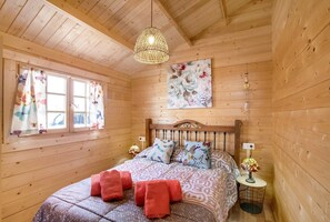 Une pièce en bois avec un lit, un luminaire suspendu, une fenêtre avec des rideaux et un tableau accroché au mur.