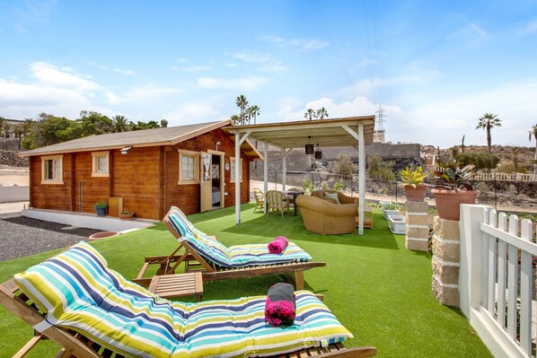 Une cabane en bois dotée d’une terrasse, de deux chaises longues, d’un espace salon abrité et offrant une vue sur le paysage environnant.