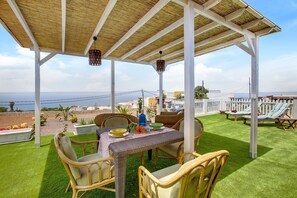 Une terrasse couverte avec une table pour deux, des chaises en osier et une vue sur la mer.