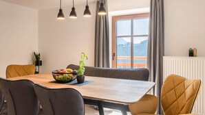 A dining area with a wooden table, grey upholstered chairs, a bowl of fruit and a potted plant, and a window with a view of a mountain. - Apartment 'Sparberhof - Floriani' with Mountain View, Open Terrace & Wi-Fi (Campo di Trens)