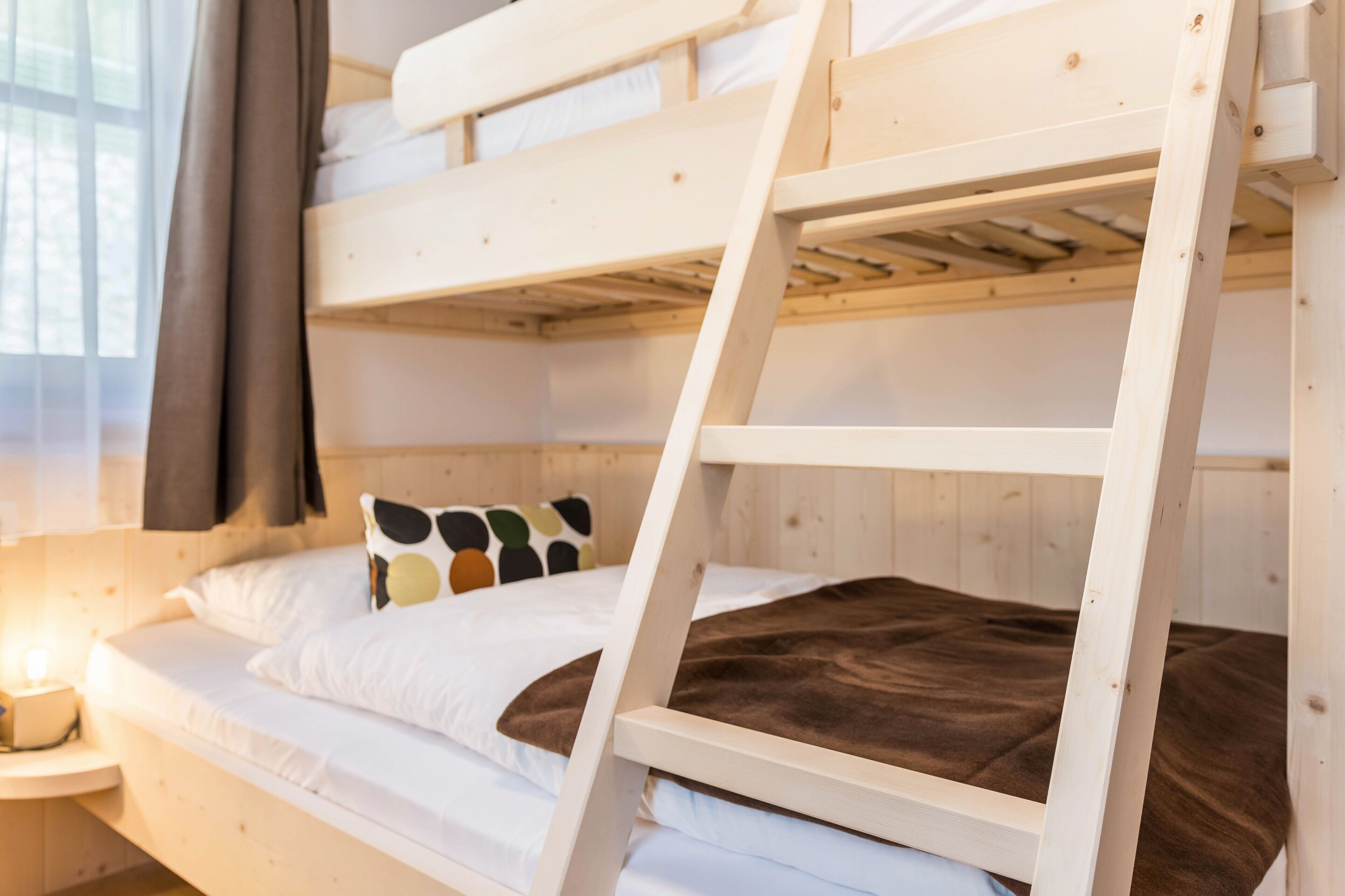 Un letto a castello con una scaletta, biancheria bianca e un cuscino con motivo multicolore.