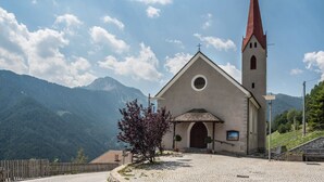 A church with a red spire, a cobblestone path, and a mountain backdrop. - Apartment 'Sparberhof - Floriani' with Mountain View, Open Terrace & Wi-Fi (Campo di Trens)
