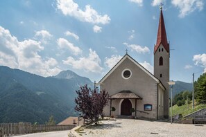 A church with a red spire, a cobblestone path, and a mountain backdrop.