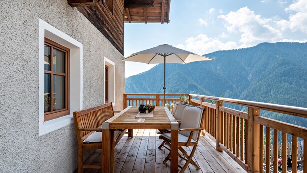 A wooden deck with a table and chairs, a large umbrella, and a mountain view. - Apartment 'Sparberhof - Floriani' with Mountain View, Open Terrace & Wi-Fi (Campo di Trens)