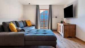 A modern living room with a sofa, a TV, a wooden cabinet, and a window with curtains. - Apartment 'Sparberhof - Floriani' with Mountain View, Open Terrace & Wi-Fi (Campo di Trens)