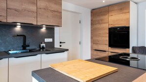 A modern kitchen with wooden cabinets, a black sink, and a built-in stove. - Apartment 'Sparberhof - Floriani' with Mountain View, Open Terrace & Wi-Fi (Campo di Trens)