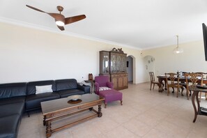 Un salon comprenant un canapé, un fauteuil, une table basse en bois, une table à manger avec des chaises et un ventilateur de plafond.