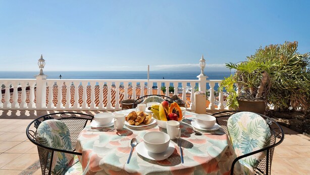 A terrace with a table set for breakfast, overlooking the sea.