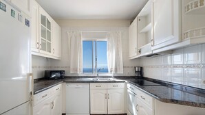 A kitchen with white cabinets, a microwave, and a view of the sea through a window.