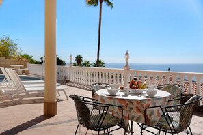 Une terrasse avec une table dressée pour le dîner, des chaises longues et une vue sur l’océan.