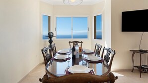A dining room with a large table set for six, a chandelier, and a TV mounted on the wall.