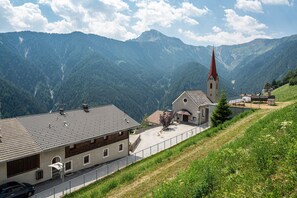 Un village de montagne avec une église, un bâtiment doté d’un toit en pente et une route où l’on aperçoit une voiture.
