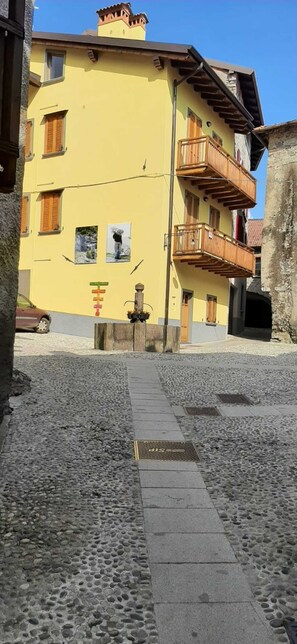 Une rue pavée menant à un bâtiment jaune doté de balcons en bois et d’un mur en pierre.