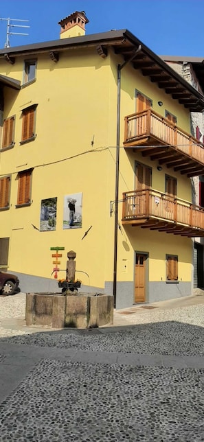 Un bâtiment jaune avec des balcons en bois, une fontaine et une rue pavée.