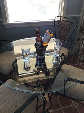 A glass-top table with a bottle and a can of beer, two glasses, and a decorative item.