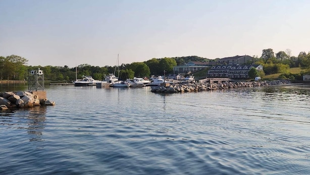 A marina with several boats docked, a large building with a sloped roof, and a rocky shoreline.