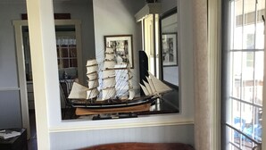 A wooden bench in a room with a large window, a wall-mounted display of model ships, and a door with a keychain.