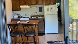 A kitchen with wooden cabinets, a central island with chairs, a ceiling fan, and a view of a balcony. - Top floor, one bedroom condo on the lake! 
 Perfect for a couples weekend. (Osage Beach)