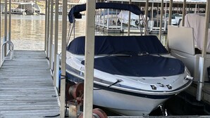 A docked boat under a covered area with a wooden deck, metal poles, and a water body in the background. - Top floor, one bedroom condo on the lake! 
 Perfect for a couples weekend. (Osage Beach)