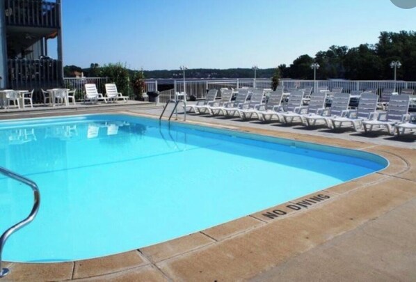 Piscina com cadeiras de espreguiçadeira e placa de 'NÃO MERGULHAR'.