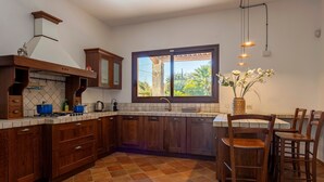 Une cuisine avec des meubles en bois, une cuisinière à gaz, une fenêtre donnant sur un beau paysage et des tabourets de bar.