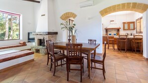 Un vaste espace dédié à la salle à manger, avec une grande table et des chaises en bois, une cheminée en pierre et une cuisine ouverte dotée de meubles en bois.