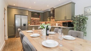 A modern kitchen with a dining area, featuring a brick backsplash, stainless steel appliances, and a large wooden table set for dining.