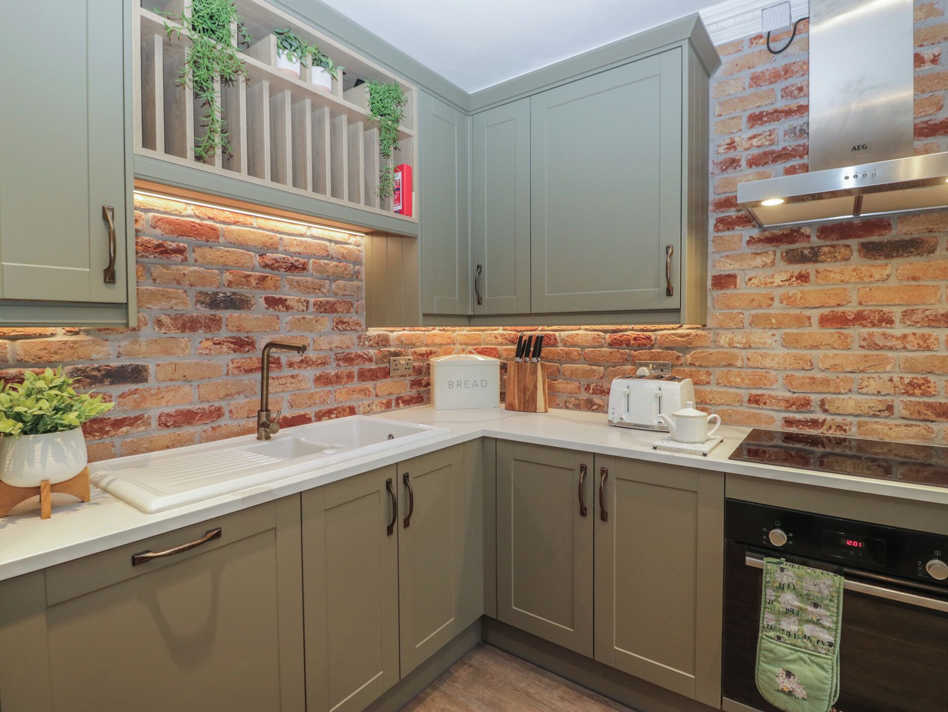 A kitchen with a brick wall, a white sink, a toaster, and a dish rack.