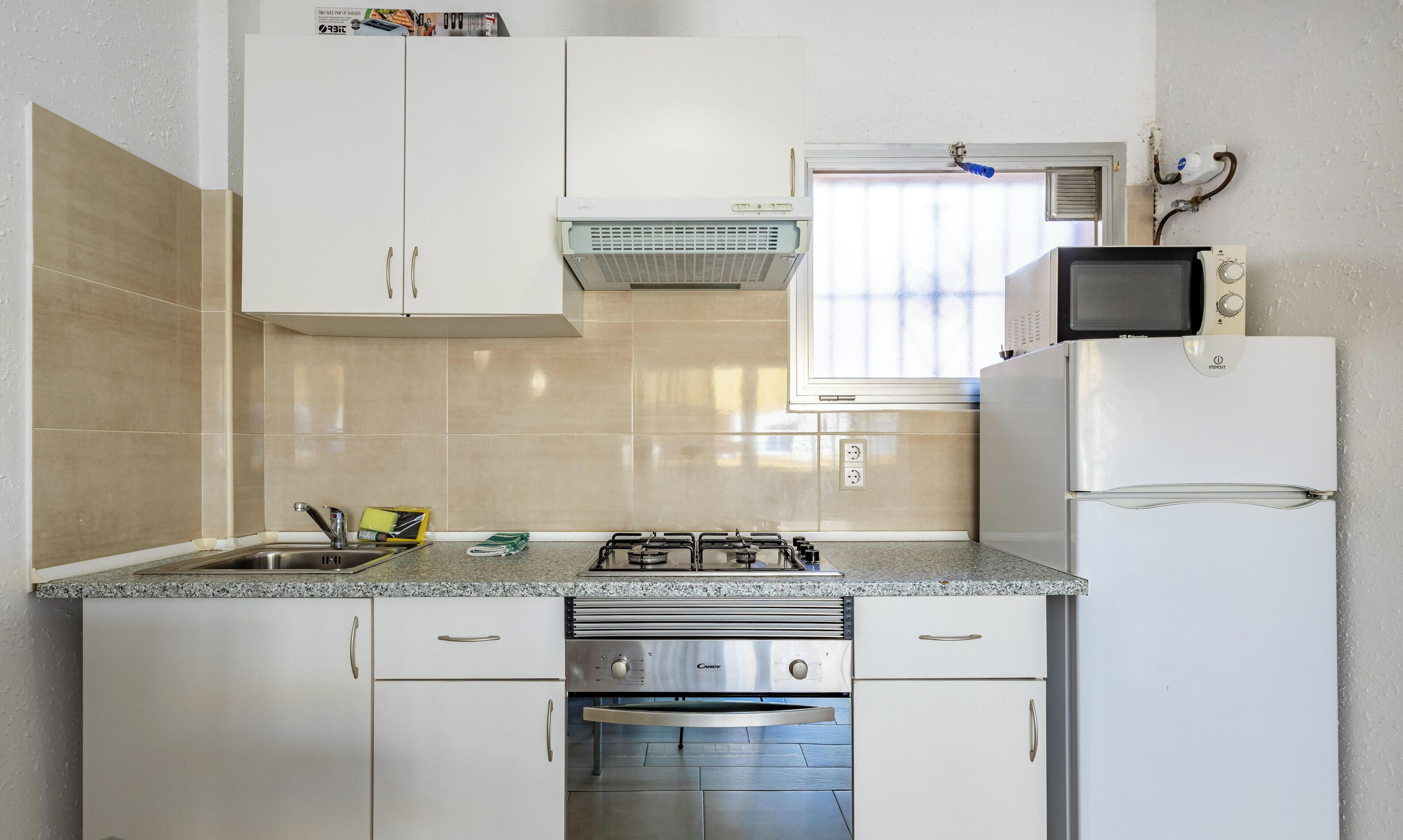 A compact kitchen with white cabinets, a gas stove, a microwave, and a refrigerator.