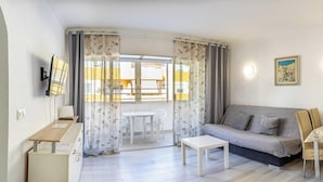 Un saló amb un sofà, una taula petita, una televisió i un balcó amb cortines.