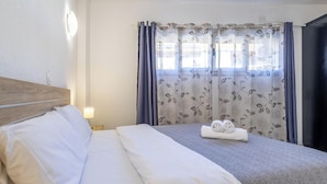 Una habitació d'hotel amb un llit ben fet, una làmpada de nit i una finestra amb cortines florals.