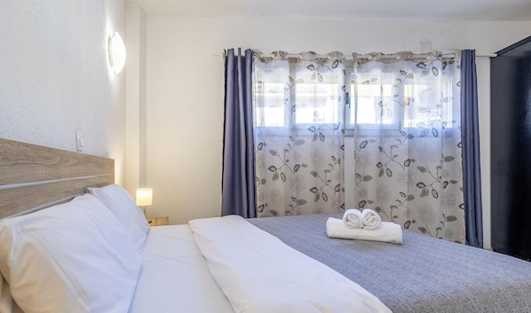 A hotel room with a neatly made bed, a bedside lamp, and a window with floral curtains.