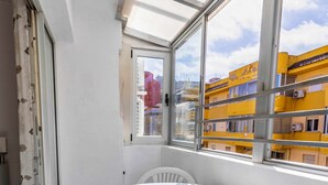 Un balcó amb una taula i caires blancs, vista d'edificis grocs i una porta oberta al mig.
