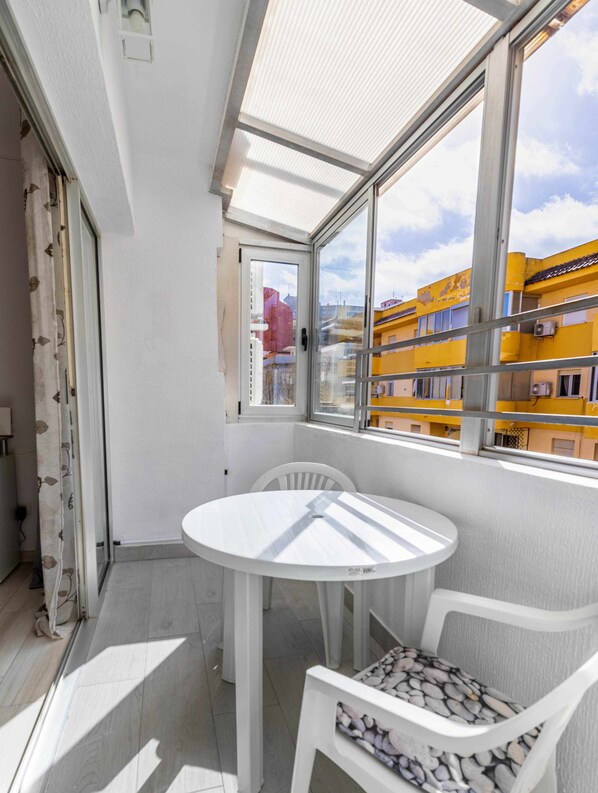 A balcony with a white table and chairs, a view of yellow buildings, and a partially open door.