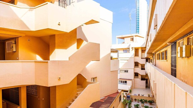 Un edifici residencial de diverses plantes amb balcons, escales i un cel serè.