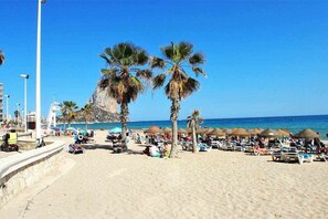 A beach with palm trees, sun loungers, and umbrellas. - Inftour Paola III Apartamento (Calp)