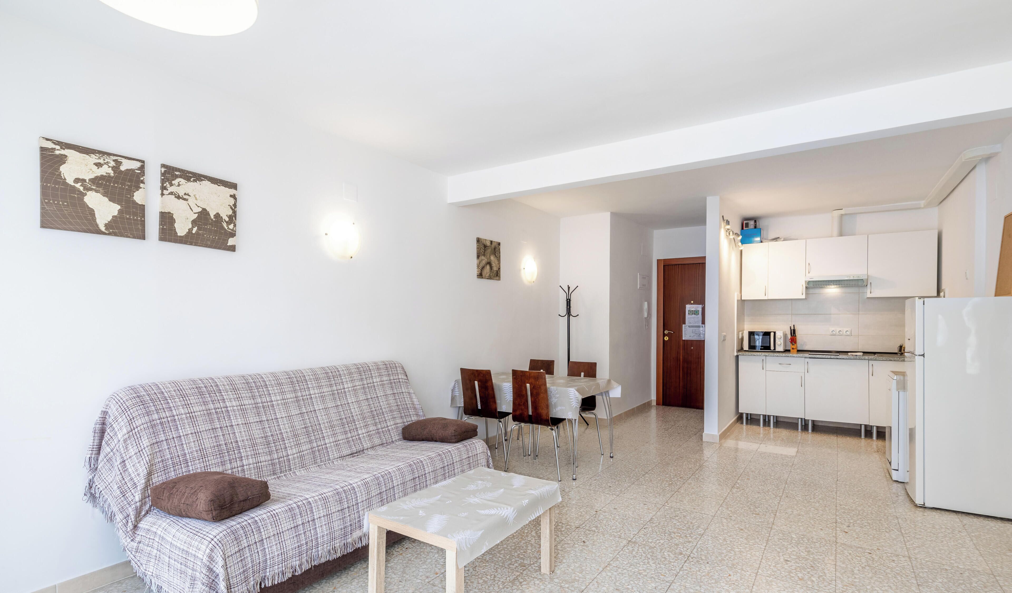 A modern apartment with a living area featuring a sofa, a dining table, and chairs. There is a kitchenette with a microwave and a refrigerator.