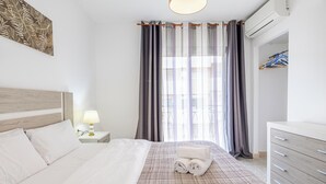 Ein Hotelzimmer mit Bett, Nachttisch mit Lampe, Kommode und einem Fenster mit Vorhängen.