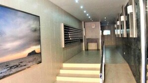 Un couloir d’hôtel moderne, avec une grande œuvre d’art sur le mur de gauche, un escalier et une rangée de luminaires au plafond.